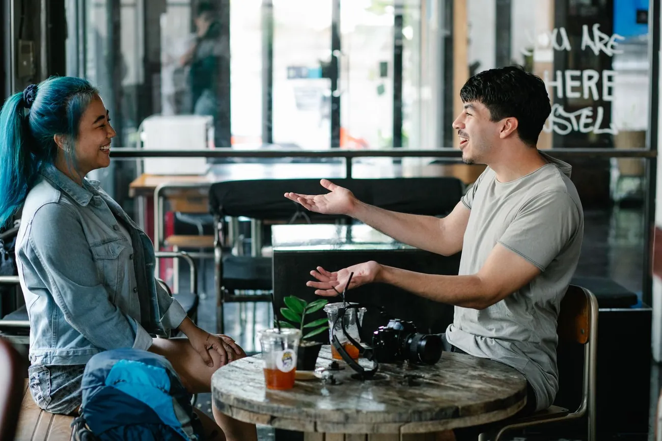 Two people sitting at a small café table, talking and laughing