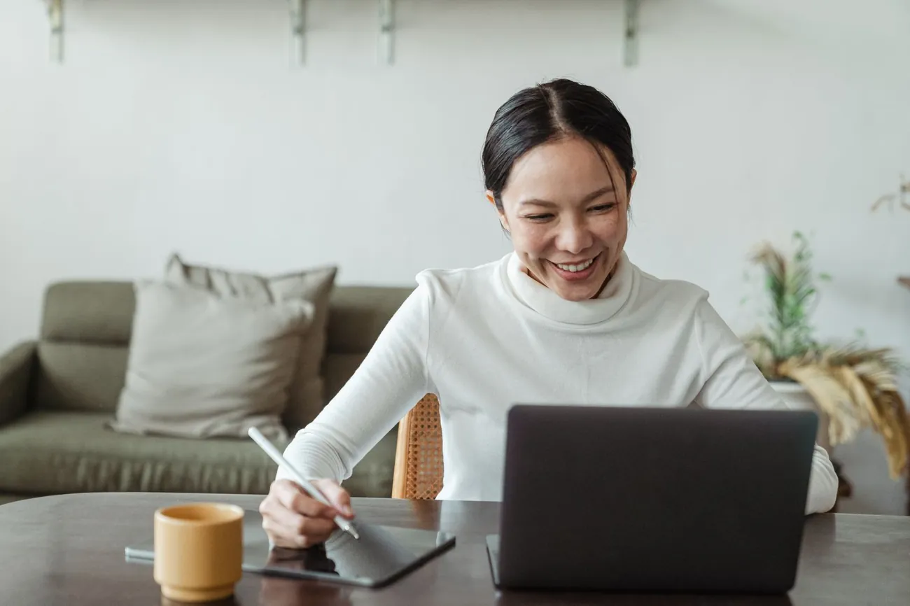A woman smiling at her laptop during a video call at a kitchen table