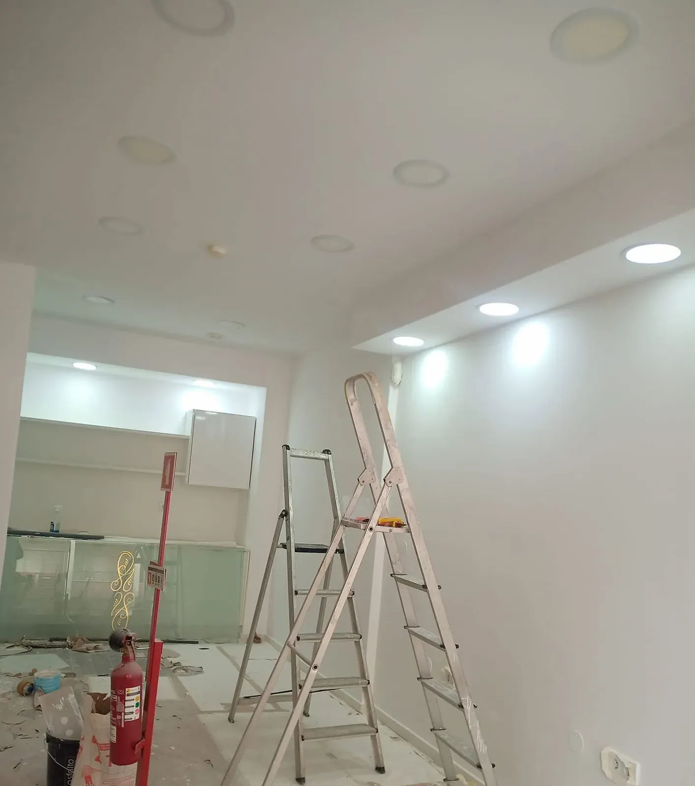 Espaço comercial em obra com focos acesos no teto falso e um escadote