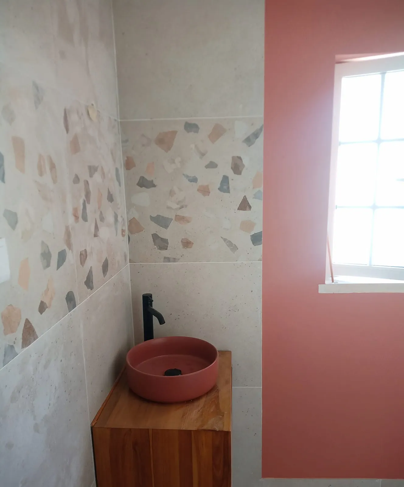 Lavatório cor de terracota sobre um móvel de madeira, com torneira alta preta e azulejo tipo marmorite