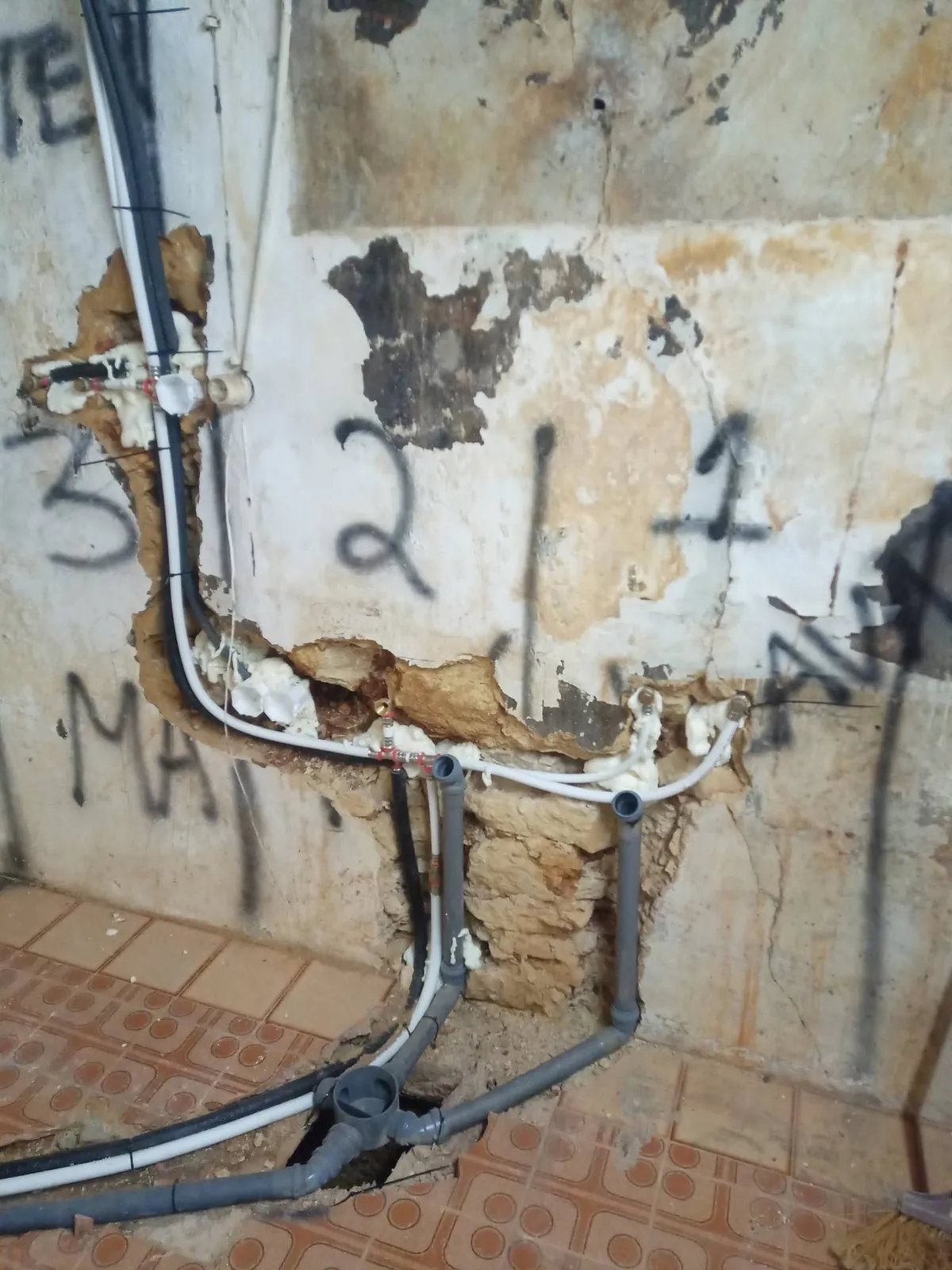 Parede antiga aberta com tubos de água e esgoto novos à vista