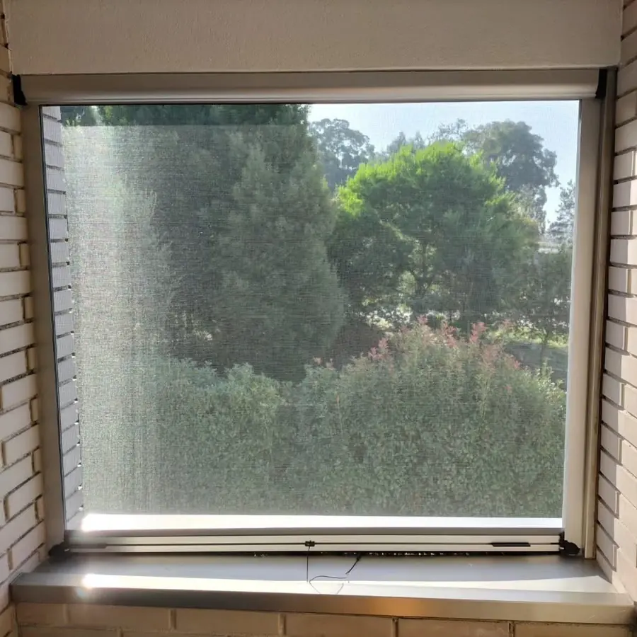 Mosquiteira de mola descida numa janela com vista para o jardim