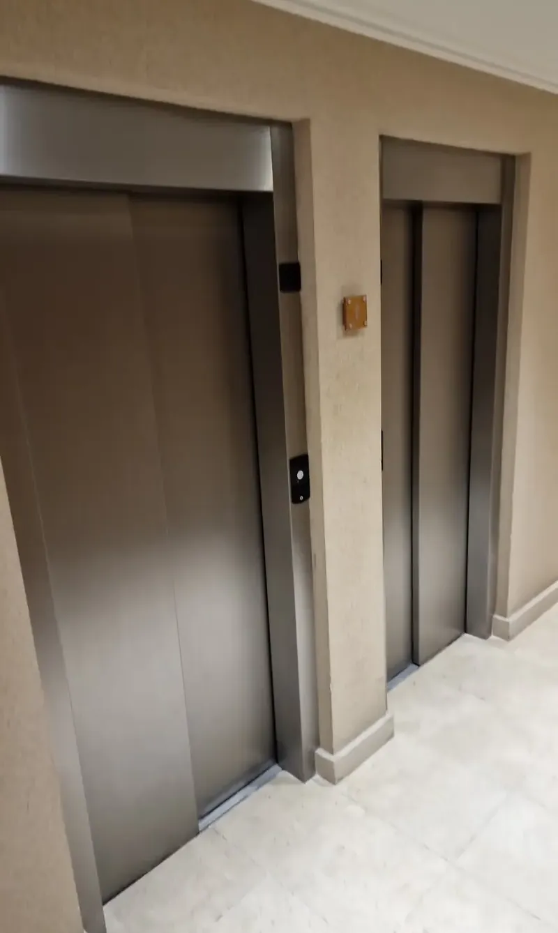 Patamar de um prédio, com as portas de dois elevadores e paredes com acabamento texturado.