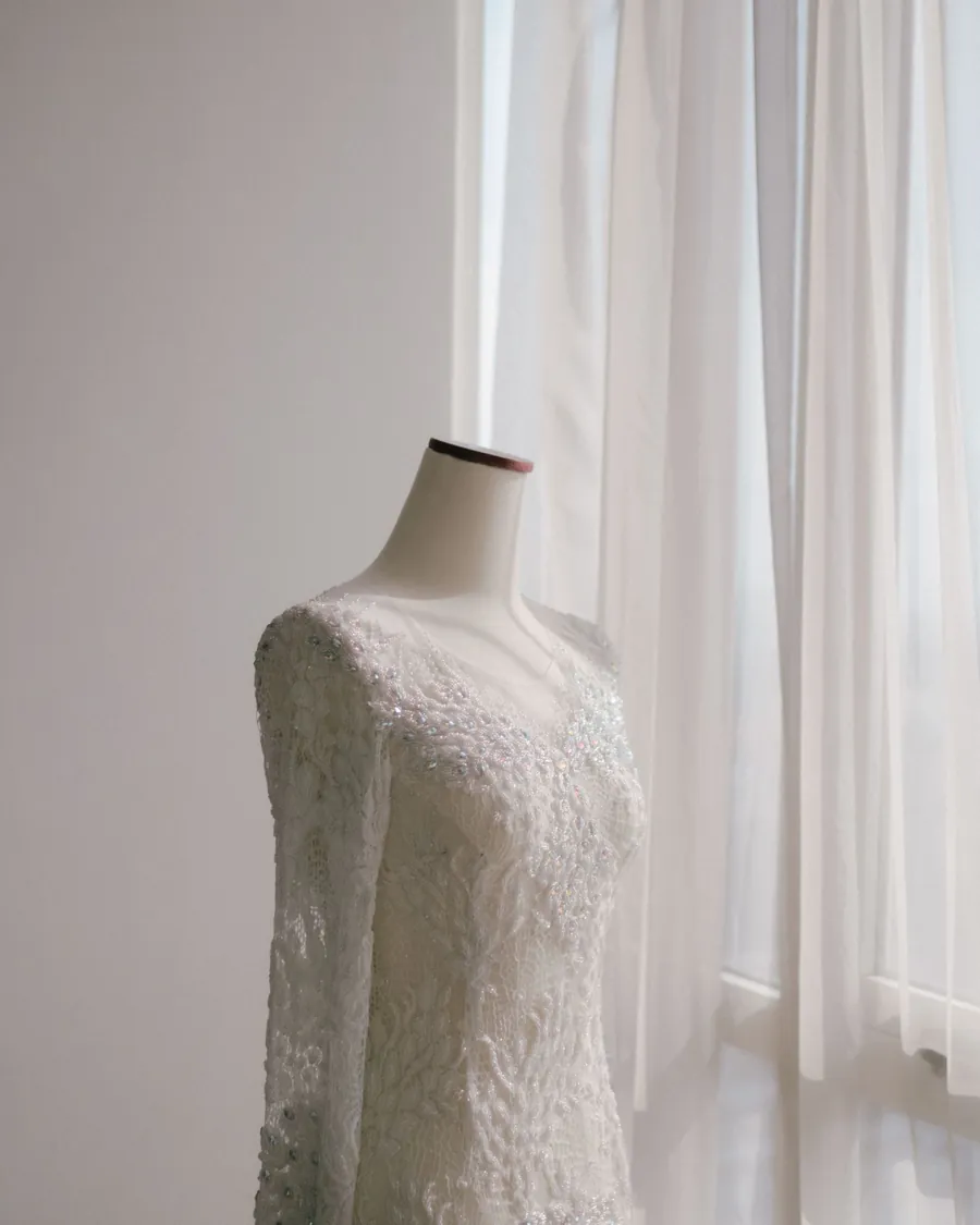 Vestido de renda de manga comprida num manequim, junto à janela.