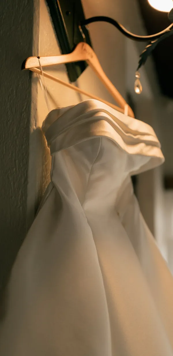 Vestido de cetim liso pendurado num cabide, à luz de um candeeiro.