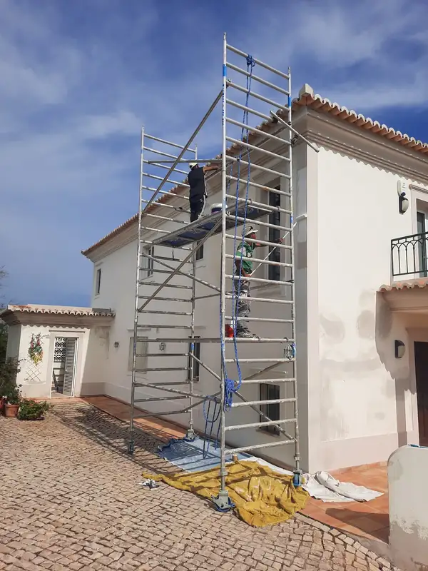 Moradia branca de estilo da região com andaime montado e técnicos a trabalhar na fachada