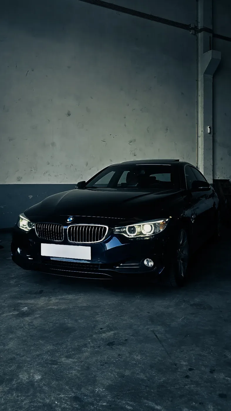 BMW Série 4 azul-escuro de faróis acesos, dentro da oficina