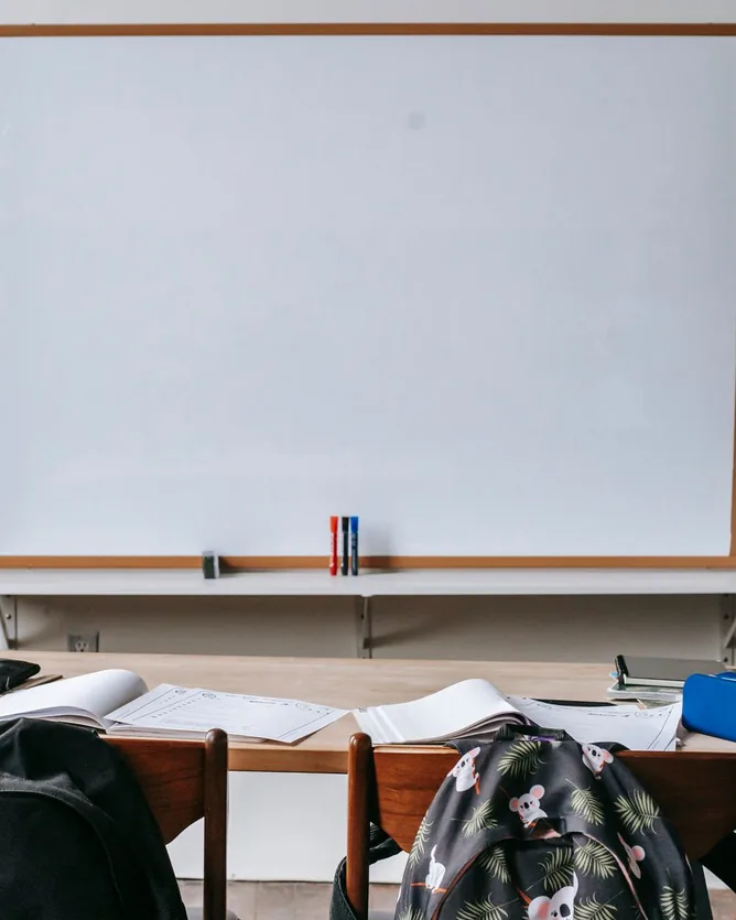 A sala das explicações: um quadro branco na parede e uma mesa com cadernos abertos, estojos e duas cadeiras com mochilas.