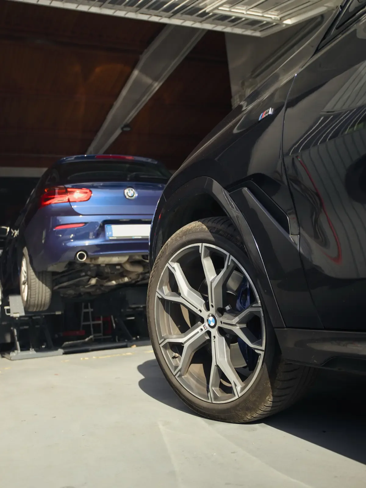 Roda de um BMW X6 em primeiro plano e um BMW Série 1 azul no elevador